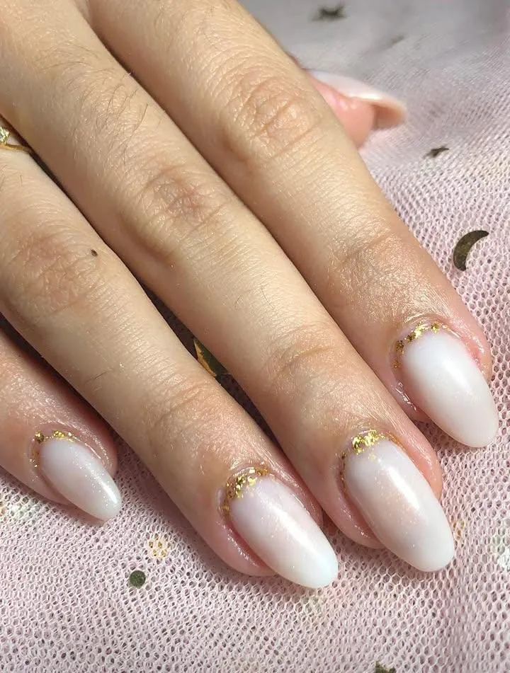 Unhas amendoadas com esmaltação branca e detalhes dourados